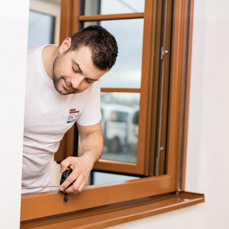 Person beim Ausmessen eines geöffneten Fensters mit einem Maßband