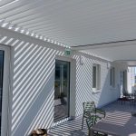 Terrasse in Klosterneuburg mit verglasten Türen, Sitzgruppen und weißer Lamellenüberdachung