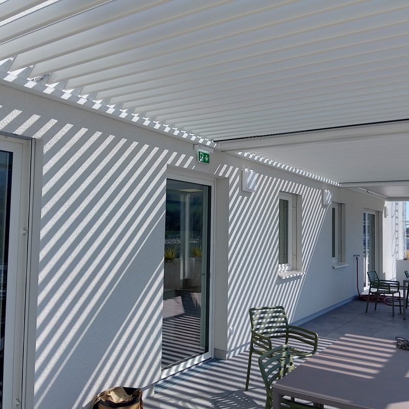 Terrasse in Klosterneuburg mit verglasten Türen, Sitzgruppen und weißer Lamellenüberdachung